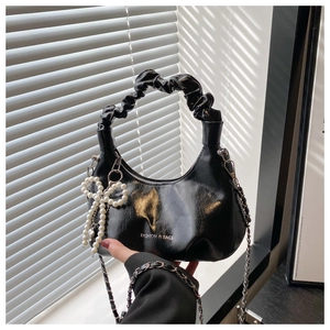 Detail of black pleated cloud bag featuring metal chain and pearl bow charm accessory