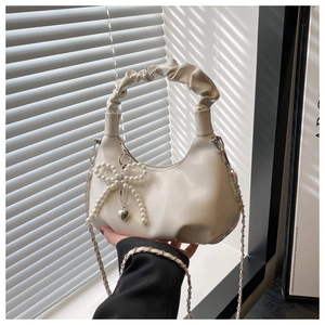 Detail of cream cloud bag featuring pearl bow charm and metal heart pendant