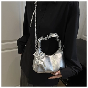 Detail of silver metallic handbag featuring ruched handle and pearl bow charm accessory