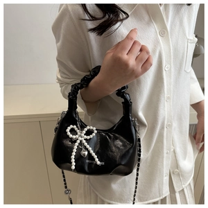 Detail of black pleated crossbody bag with pearl bow and metal heart charm on a model