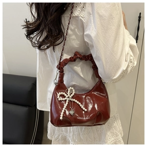 Detail of burgundy glossy handbag with ruched handle and pearl bow charm accessory