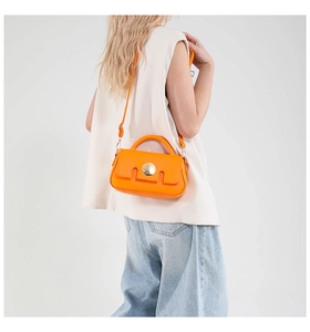 Chic orange crossbody bag with gold hardware worn by a model in a white studio setting