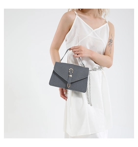 Detail of grey crossbody bag with woven texture and gold metal clasp on white dress
