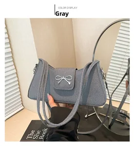 Detail of grey denim baguette bag featuring a silver metal bow and slim shoulder strap