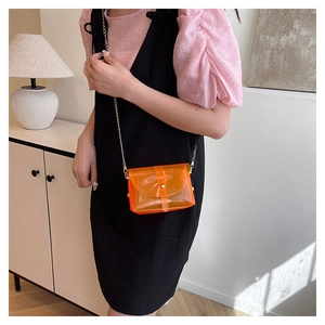 Détail du sac transparent orange avec chaîne dorée porté par un mannequin à l'épaule