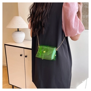 Detail of a green transparent PVC envelope bag with gold chain strap on a model