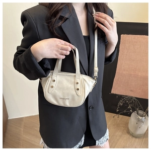 Detail of cream crossbody bag with gold hardware and logo shown with a black blazer