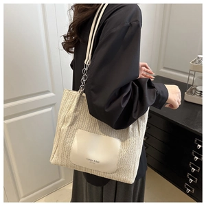 Close-up of beige woven tote bag featuring white leather patch and silver chain detail