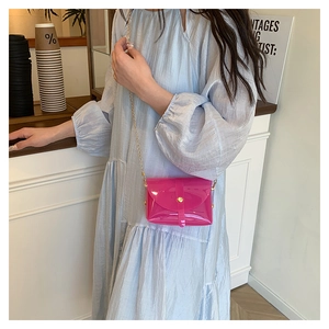 Detail van rozerode PVC crossbodytas met gouden ketting gedragen door een model