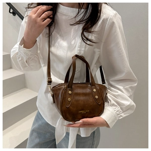 Detail of dark brown leather bucket bag with gold studs and shoulder strap on a model