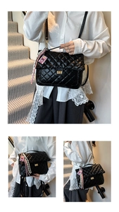 Detail of black quilted shoulder bag with gold square twist lock and tassel charm
