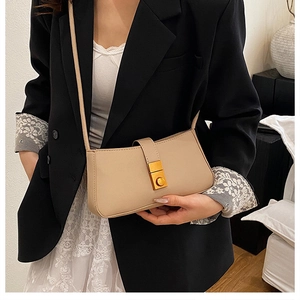 Detail of a chic beige leather crossbody bag with gold clasp worn over a black blazer