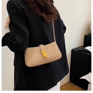 Detail of a beige baguette shoulder bag with a gold metal push-lock on a model