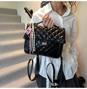 Close-up of quilted black leather tote featuring a gold twist lock and a pink charm