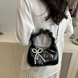 Black ruched cloud handbag with pearl bow and heart pendant in a stylish indoor setting