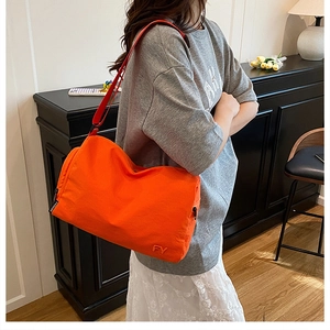 Détail du sac bandoulière en nylon orange vif avec broderie FY et sangle mode sur mannequin