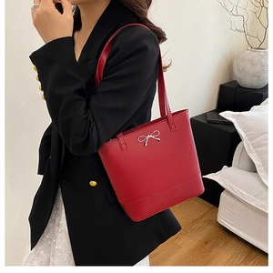 Détail du sac cabas rouge avec nœud argenté porté par un mannequin en tailleur
