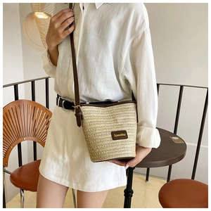 Detail of woven straw bucket bag with contrast leather strap and brand patch