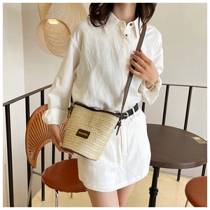 Close-up of straw woven bucket bag with brown leather trim and shoulder strap detail