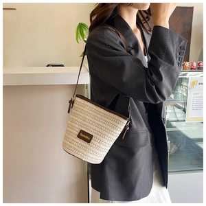 Close-up of beige woven bucket bag with brown leather trim and shoulder strap details
