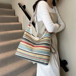 Colorful woven tote bag with rainbow stripes and white shoulder strap worn by a model