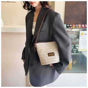 Detail view of woven straw bucket bag with brown leather base and adjustable strap
