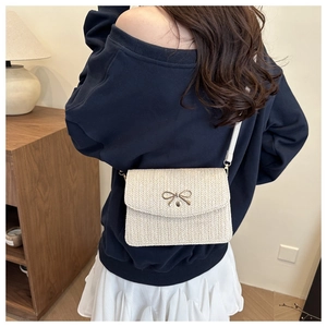 Close-up of cream woven crossbody bag featuring a golden butterfly metal clasp detail