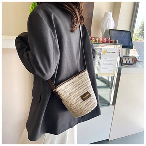 Detail of beige woven bucket bag featuring brown leather trim and crossbody strap