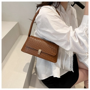 Detail of a brown shoulder bag with woven embossed texture and silver metal buckle