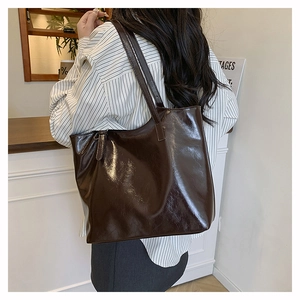 Shoulder view of a dark brown glossy leather tote bag with thin straps and minimalist design