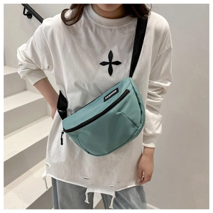 Detail of light green crescent nylon chest bag featuring adjustable black strap and fashion tag