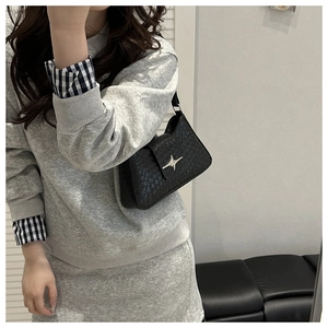 Close-up of a woven black shoulder bag with a silver star buckle on a model