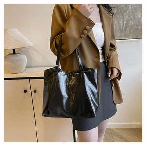 Detail of glossy black tote bag with double shoulder straps and metal buckle on the strap