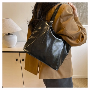 Detail of glossy black tote bag with metal buckle on shoulder strap and leather finish