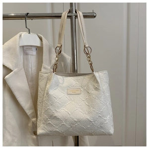 Detail of cream tote bag featuring textured fabric and a gold chain strap on display
