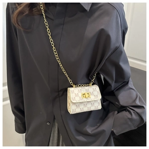 Detailed view of cream micro bag with M-pattern and gold chain strap on black shirt