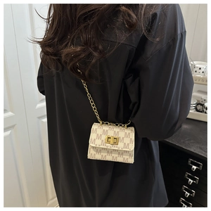Detail of a mini cream crossbody bag with brown M print and golden chain strap on a model