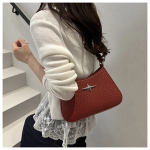 Détail du sac rouge tissé avec étoile en métal porté sur un escalier blanc épuré