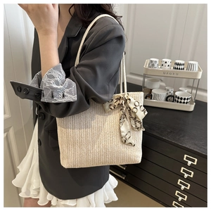 Detail of woven straw tote bag with elegant silk scarf on handle for summer style