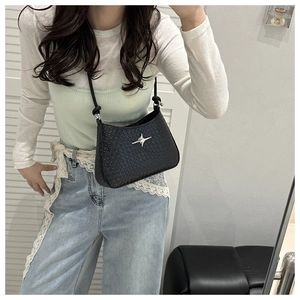 Close-up of black woven shoulder bag with silver star metallic detail worn by a model