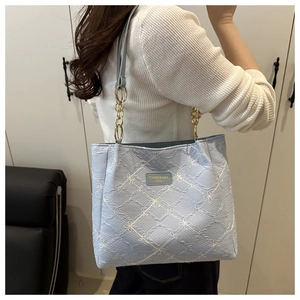 Detail of light blue quilted tote bag with floral embroidery and gold chain strap