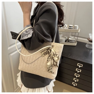 Detail of straw tote bag showing beige woven texture and decorative silk scarf accent