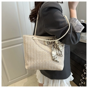 Détail d'un sac en paille beige avec anses en corde épaisse et foulard en soie à motifs chic