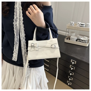Sac bandoulière blanc chic avec nœud et boucles argentées porté par un mannequin