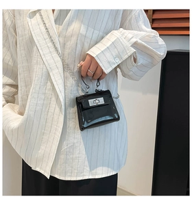 Detalle de un mini bolso de charol negro con hebilla plateada tipo bandolera
