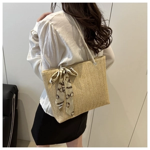 Detail of woven straw tote bag with chain-patterned silk scarf bow and white straps