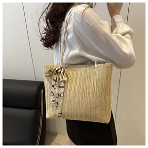 Detail of light beige straw tote bag featuring decorative silk scarf and long shoulder strap