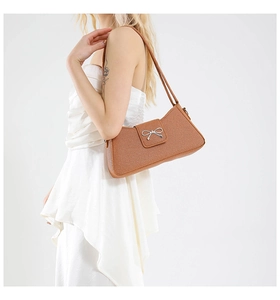 Brown textured baguette shoulder bag with silver bow clasp on white dress model