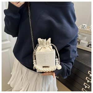 Close-up of cream crossbody bag with pearl handle, chain strap, and snake texture detail