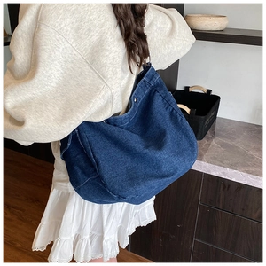 Détail d'un grand sac bandoulière en denim bleu marine porté par un mannequin à l'épaule
